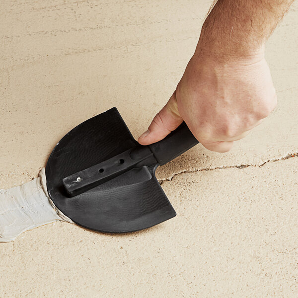 A person using a Midwest Rake flexible radius trowel to remove a crack in cement.