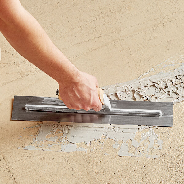 A person using a Midwest Rake epoxy mortar trowel to put cement on the floor.