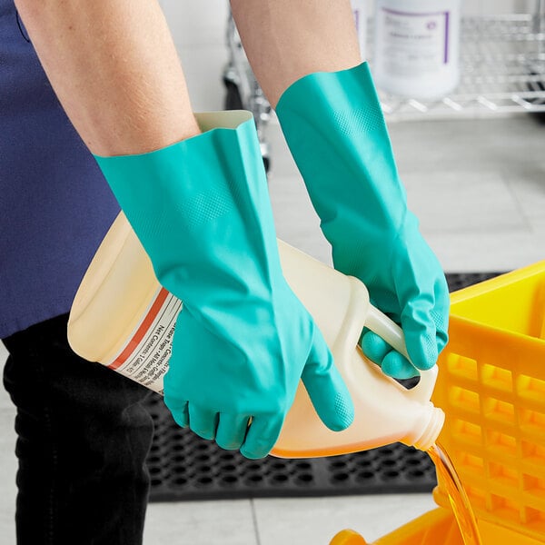 A person in green Midwest Rake Solvent-Resistant Nitrile gloves holding a jug of cleaning liquid.