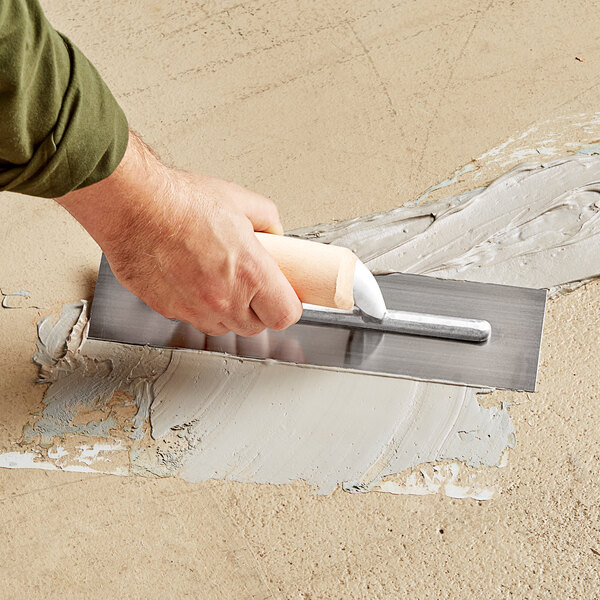 A person using a Midwest Rake epoxy mortar trowel on a floor.