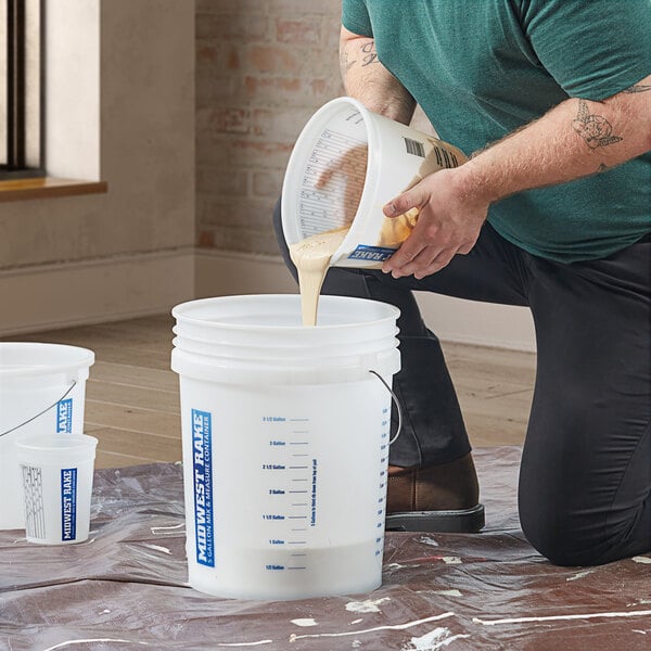 A man pouring a white plastic container of liquid into a white bucket.