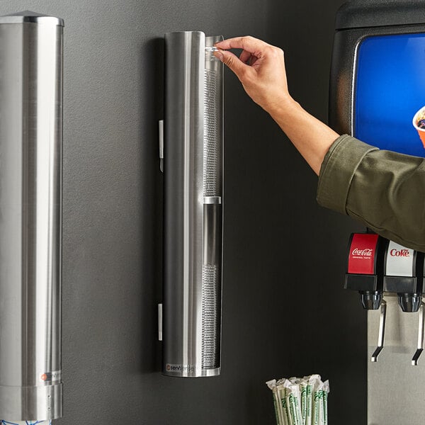 A person using a ServSense stainless steel lid organizer to dispense a coffee cup.