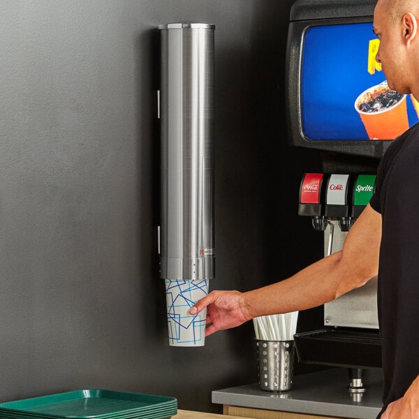 A man using a stainless steel wall-mounted cup dispenser.