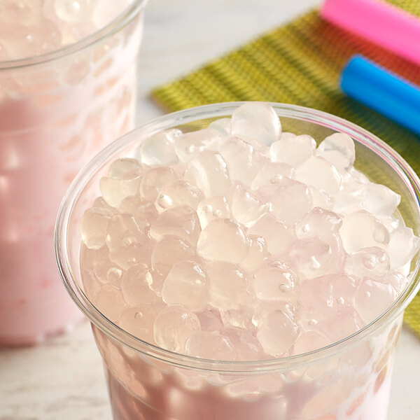 A glass of pink liquid with a straw and a close-up of Bossen Lychee Crystal Boba in Syrup.