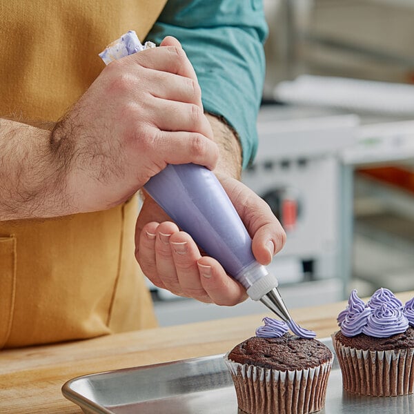 A person using a Choice clear disposable pastry bag to pipe purple frosting onto a cupcake.