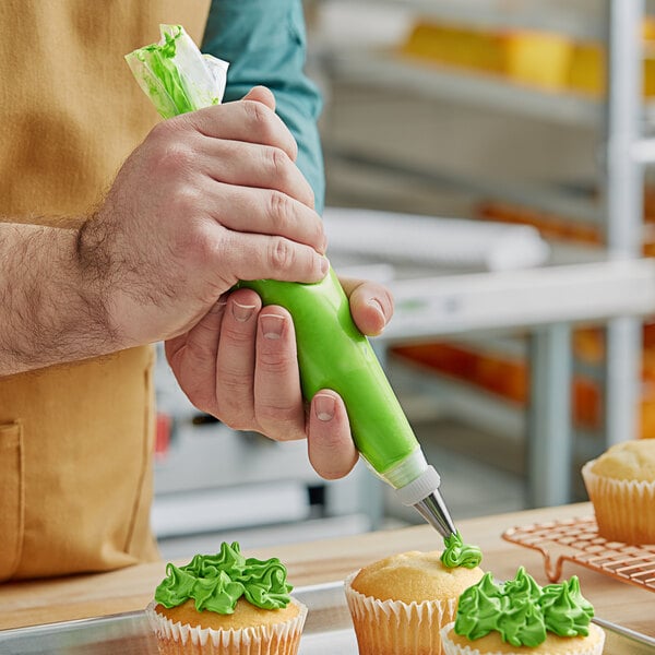 A hand using a green Choice pastry bag to frost a cupcake.