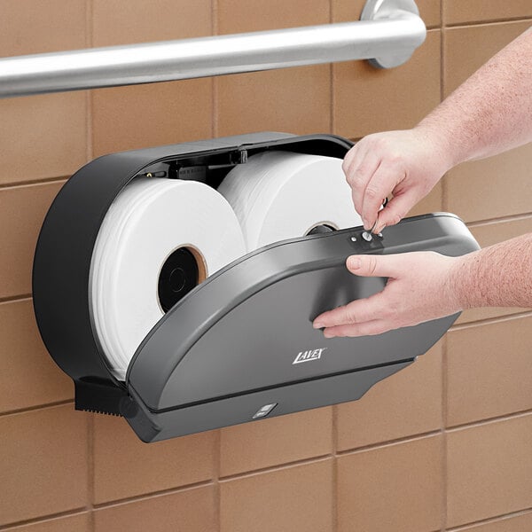 A hand using a Lavex double roll jumbo toilet paper dispenser.