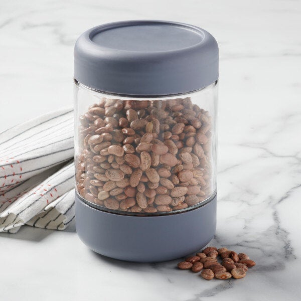 A stackable glass jar with a threaded lid, filled with beans.