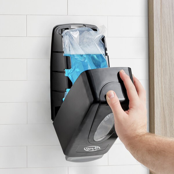 A hand pressing a black Noble Chemical foam hand soap dispenser.