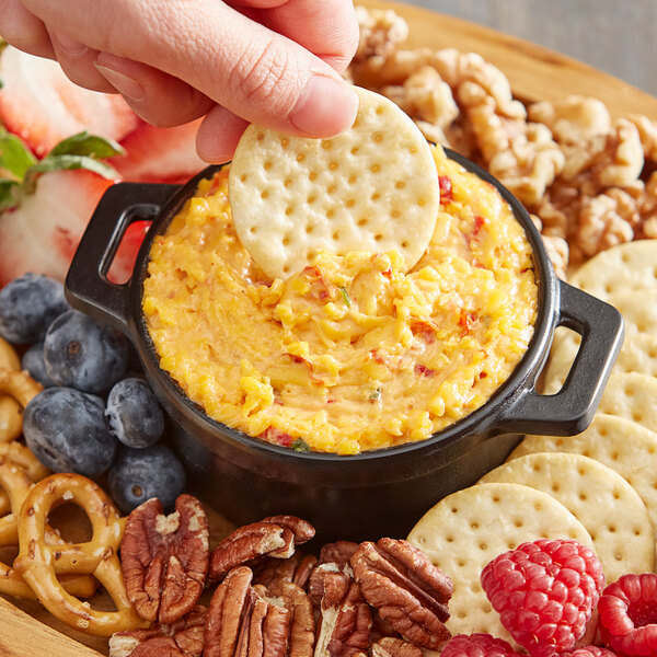 A person dipping a cracker into a bowl of Don's Salads Southern-Style Pimento Cheese Spread.