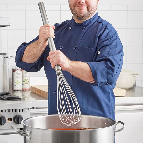 A man in a chef's uniform using a Fourté stainless steel French whisk in a pot.