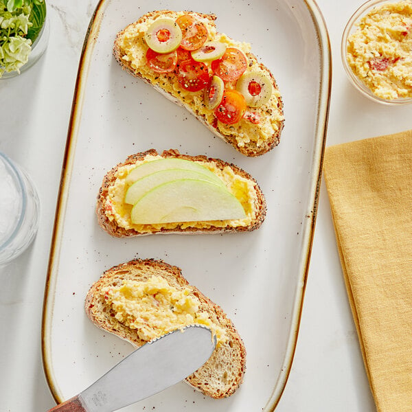 A knife spreading Melanie's Medleys Pimento Cheese Dip on a piece of bread.