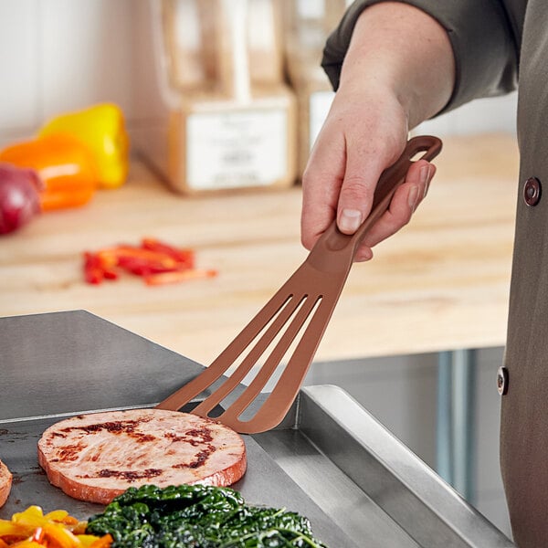 A hand holding a brown Mercer Culinary Hell's Tools spatula over a pan of food.