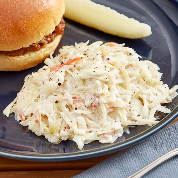 A plate with coleslaw and a sandwich on a table with a burger.