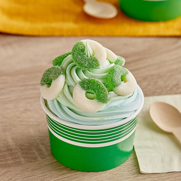 A cup of ice cream with green and white candy rings on top.