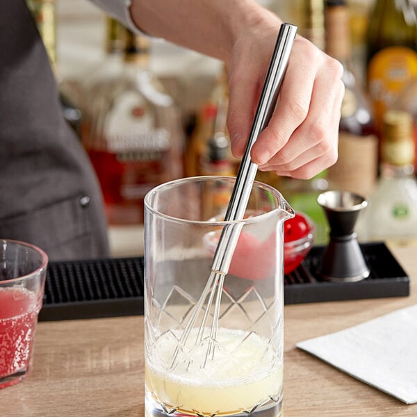 A Choice stainless steel mini whisk in a glass cup.