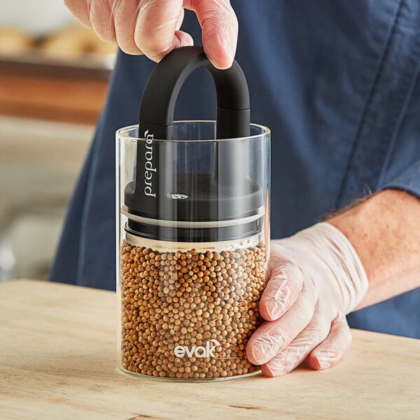 A person using a Prepara Evak Classic glass food storage container to pour seeds into it.