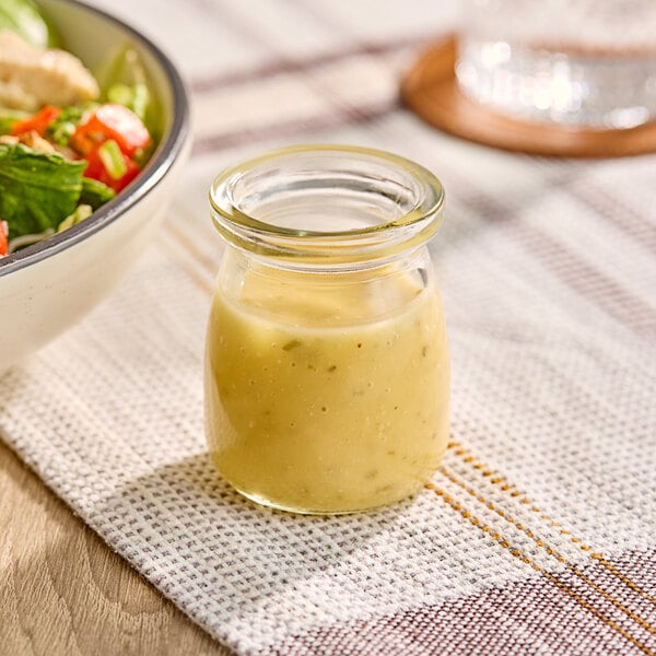 A small round glass jar with a 4 oz. capacity, shown filled with a light-colored dressing.