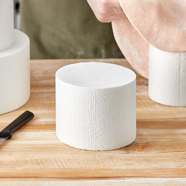 A person cutting a Baker's Lane foam round cake dummy with a knife.