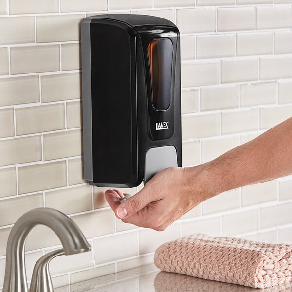 A hand holding a Lavex black manual liquid soap dispenser.