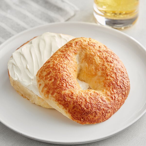 A Just Bagels asiago bagel with cream cheese on a white plate.