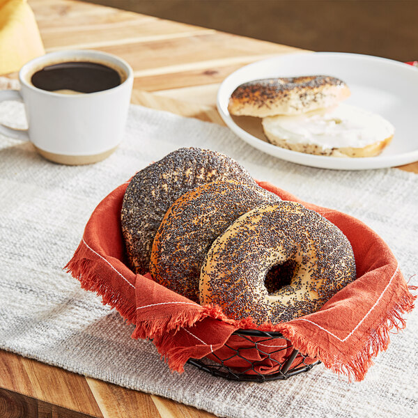 A bagel with poppy seeds in a basket next to a cup of coffee.