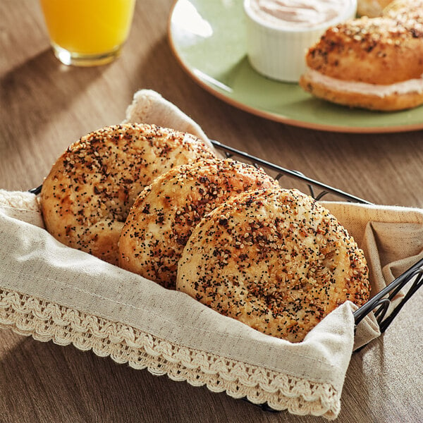 A basket of Just Bagels New York Everything Bagels with seeds, one cut open to show black and white specks.