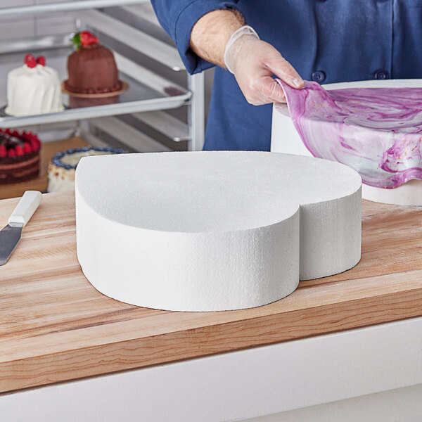 A person cutting a foam heart cake dummy with a knife.