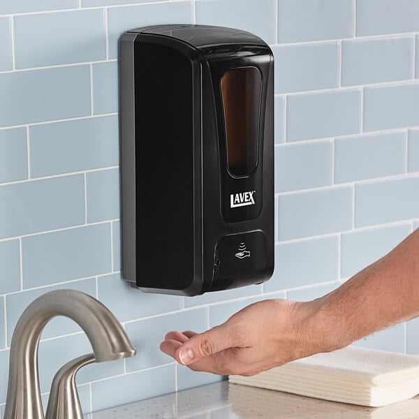 A person using a black Lavex automatic liquid soap dispenser on a wall above a sink.