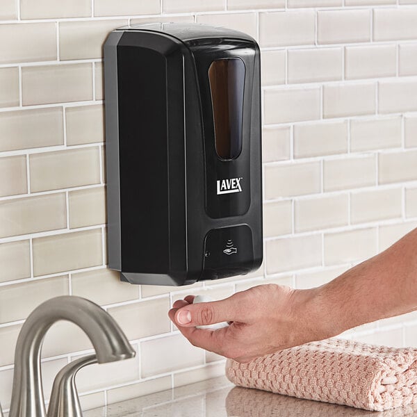 A person using a black Lavex automatic foaming soap dispenser.