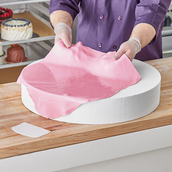 A person in purple gloves using a Baker's Lane foam round cake dummy to make a pink cake.