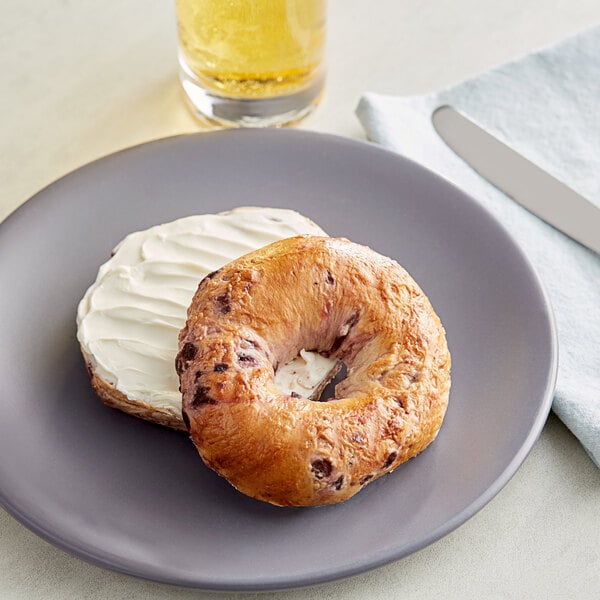 A Just Bagels blueberry bagel with white frosting on a plate with a knife.