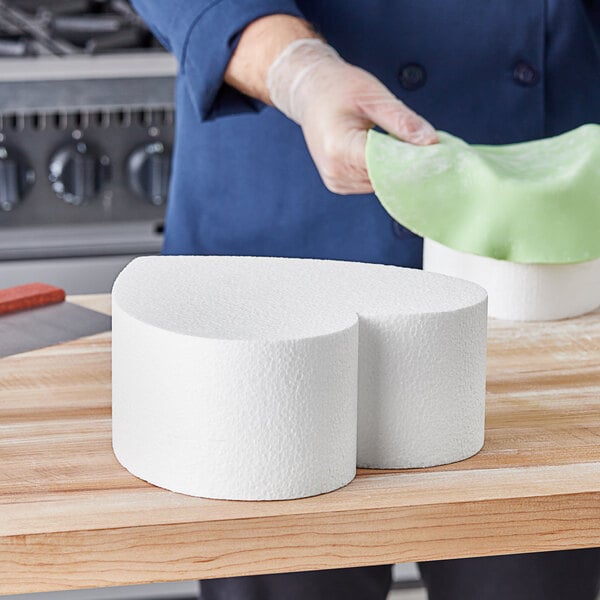 A person using a Baker's Lane foam heart cake dummy to prepare a cake.