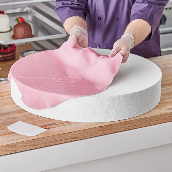 A person in a purple shirt using a Baker's Lane foam round cake dummy to prepare a cake.