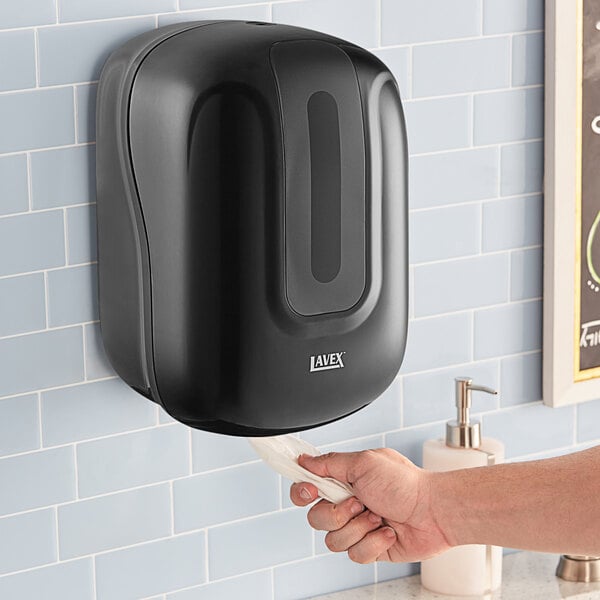 A person's hand using a black Lavex center pull paper towel dispenser on a wall.