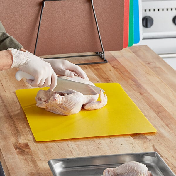 A person cutting a chicken on a Choice multi-colored flexible cutting board.