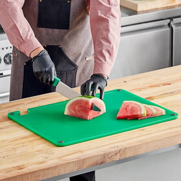 A person cutting a watermelon on a green Choice cutting board.