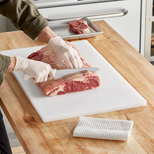 A person in gloves cutting meat on a white Choice polyethylene cutting board.