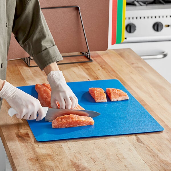 A person cutting salmon on a multi-colored flexible cutting board on a counter.