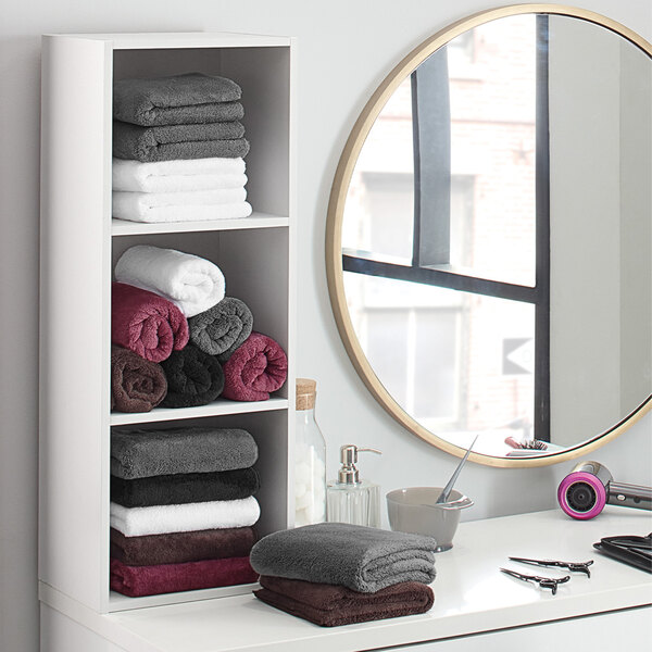 A shelf with Monarch Brands brown hand towels and a mirror.