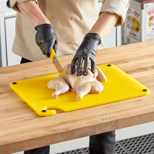 A person in gloves using a knife to cut a chicken on a yellow Choice cutting board.
