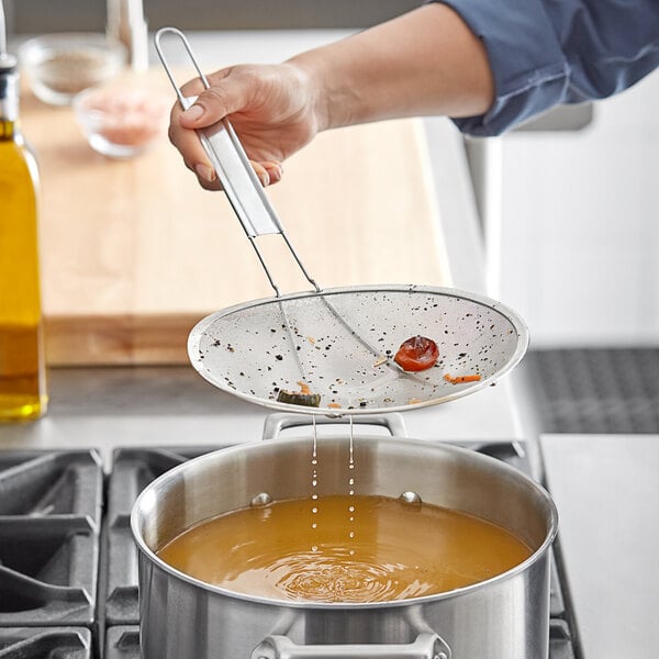 A person using a Choice extra fine mesh skimmer to pour liquid into a pan.