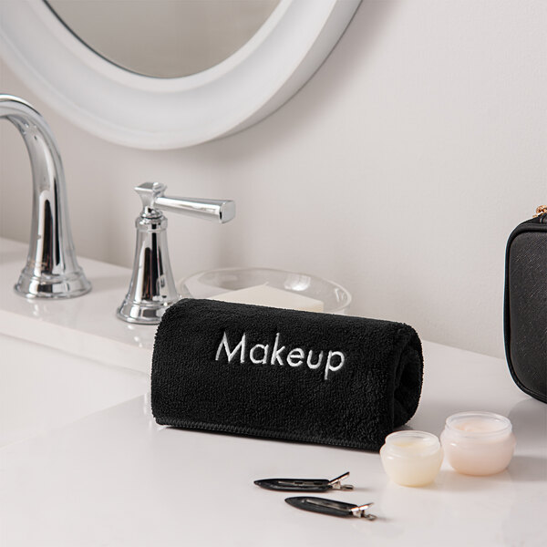 A black Monarch Brands coral fleece towel with white text on a bathroom counter.