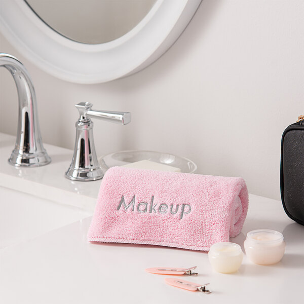 A pink Monarch Brands coral fleece towel next to a mirror with a black makeup bag.