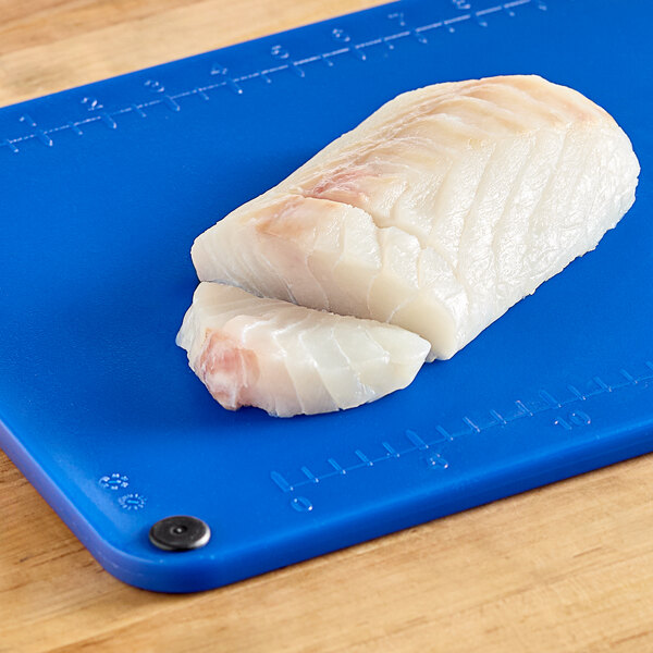 A piece of white fish on a blue Choice cutting board with rulers and grips.