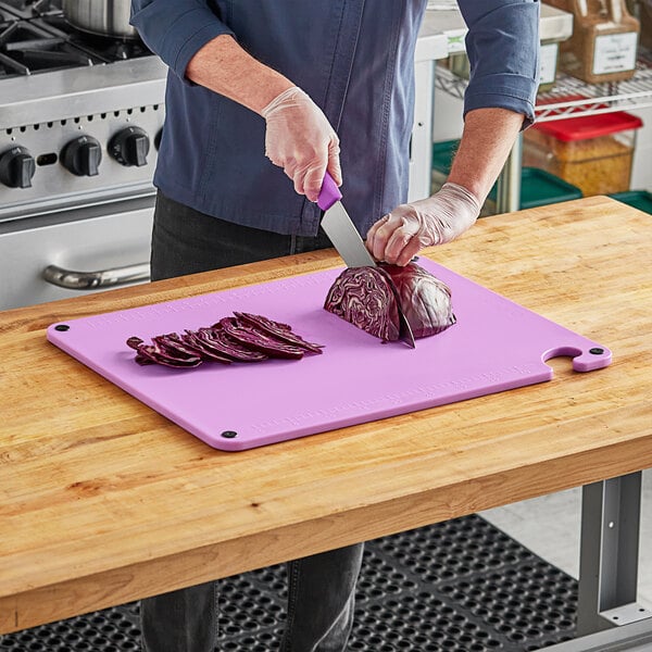 A person cutting a red cabbage on a purple Choice cutting board.