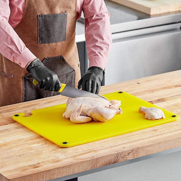 A person wearing gloves uses a yellow Choice cutting board to cut up a chicken.