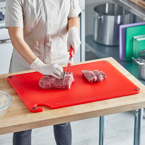 A woman cutting meat on a Choice red cutting board.