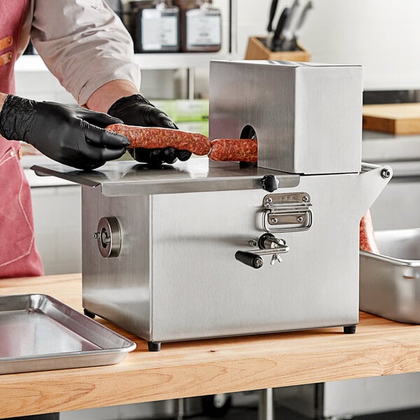 A person in black gloves using a Backyard Pro sausage tying machine to tie a sausage on a metal tray.