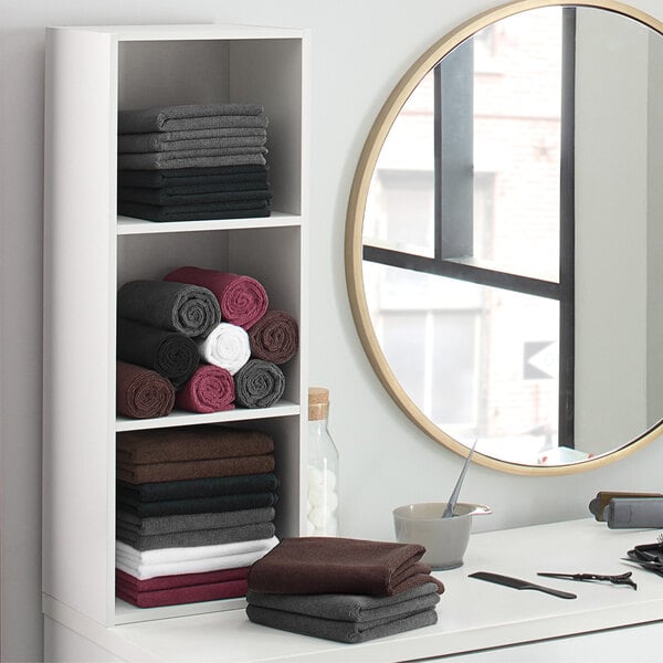A shelf with Monarch Brands brown hand towels and a mirror.